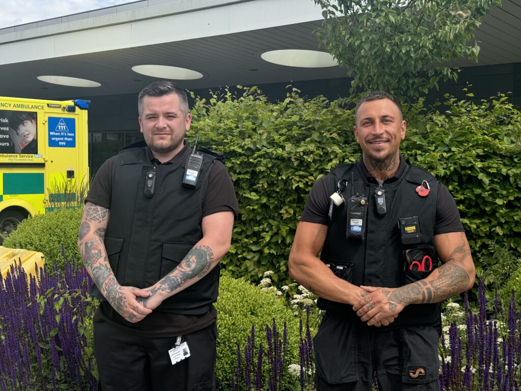 Two members of security staff standing outside a hospital entrance.