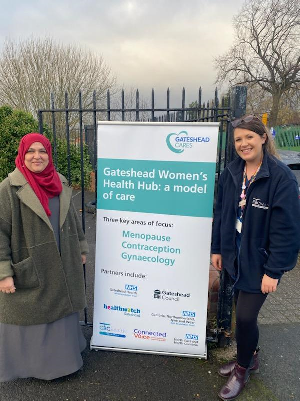 Photo of 2 staff members from the community health bus, with a sign advertising the services, which include menopause, contraception and sexual health screening.