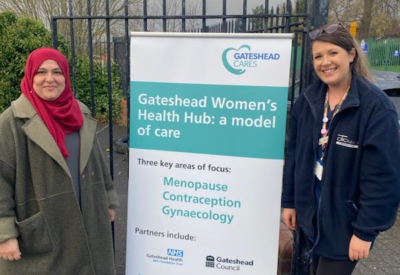 Photo of 2 staff members from the community health bus, with a sign advertising the services, which include menopause, contraception and sexual health screening.