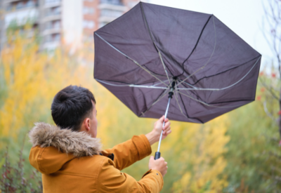 A person in a yellow coat holding an umbrella in windy weather